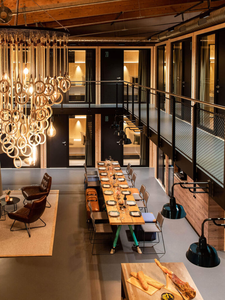 Modern eingerichteter Essbereich mit langer Tafel, Lounge-Sesseln und stilvoller Beleuchtung in warmem Ambiente.