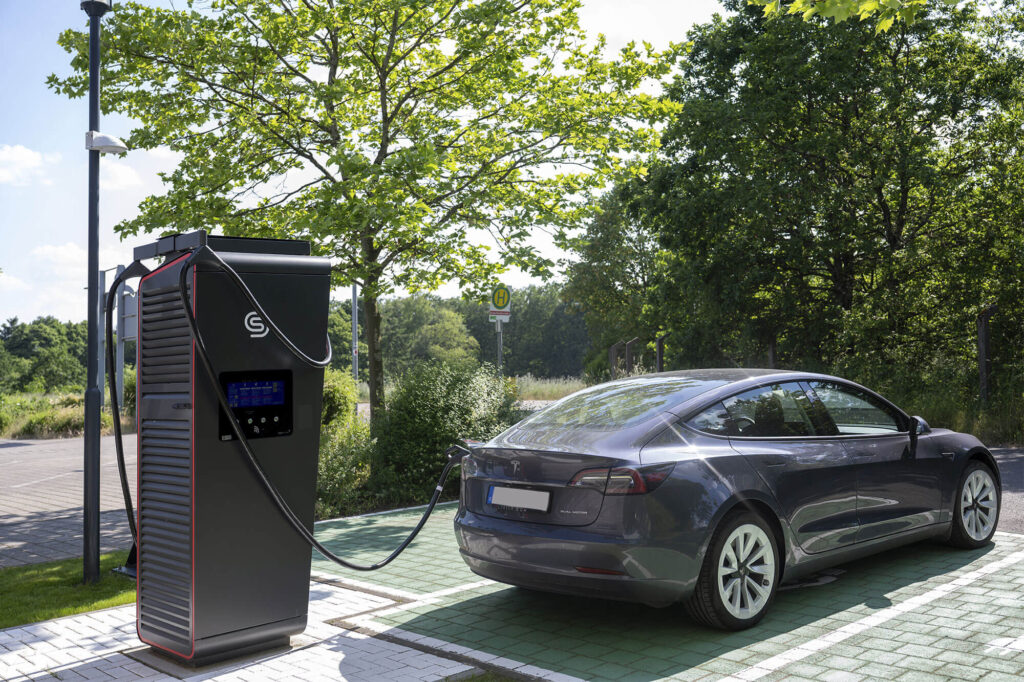 Ein Elektroauto lädt an einer modernen Ladestation im Grünen bei sonnigem Wetter.