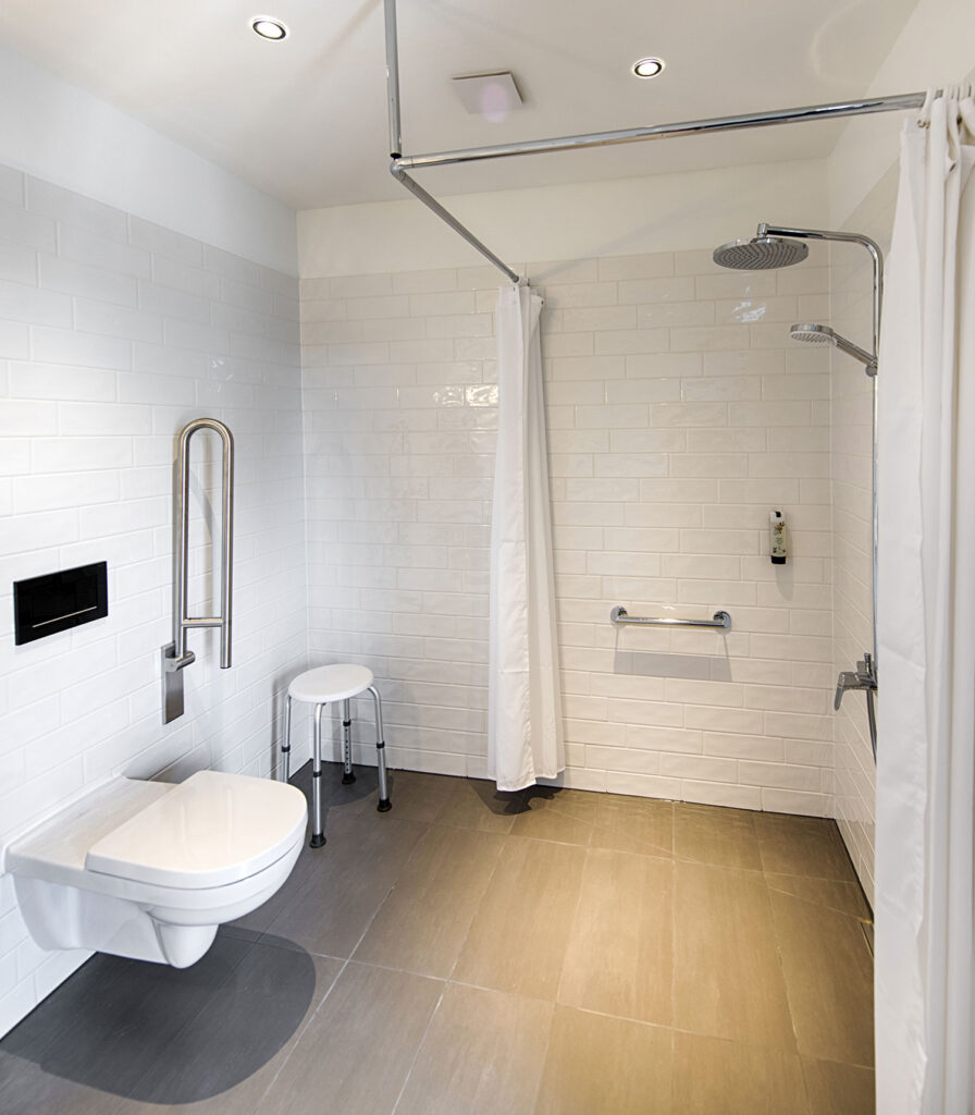 Barrierefreies Bad mit bodengleicher Dusche, Duschsitz, Haltegriffen und wandhängendem WC.